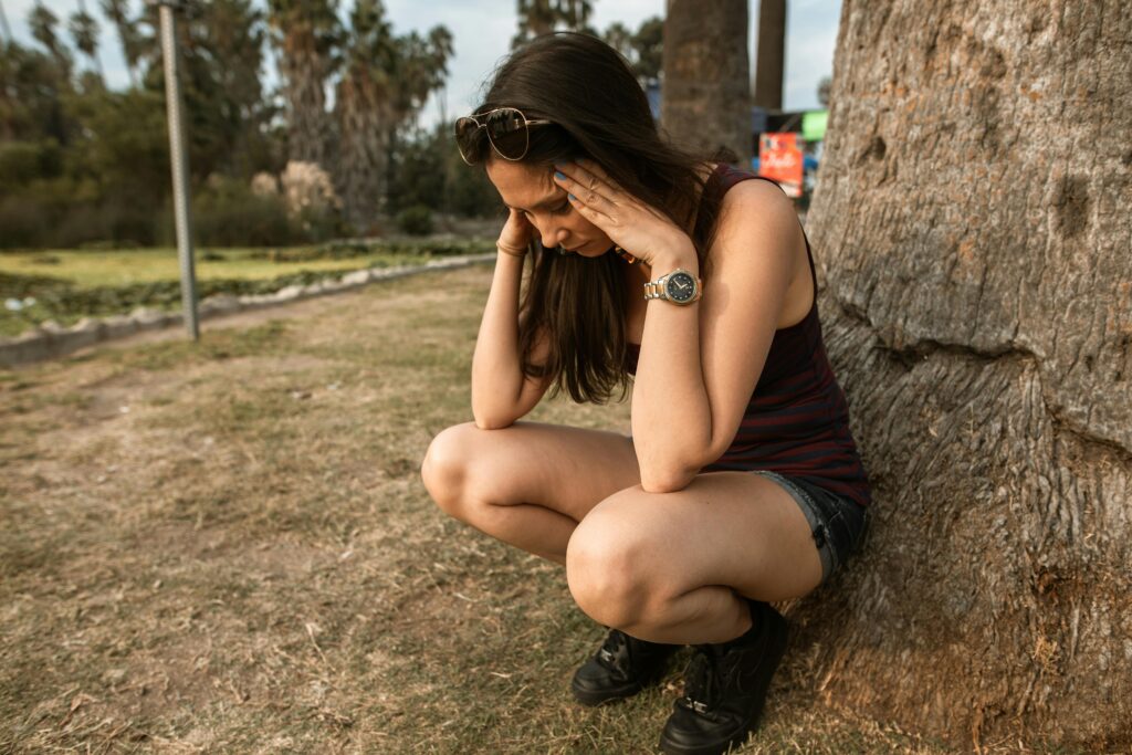 Woman undergoing anxiety attack kneeling by a tree trying to calm herself down